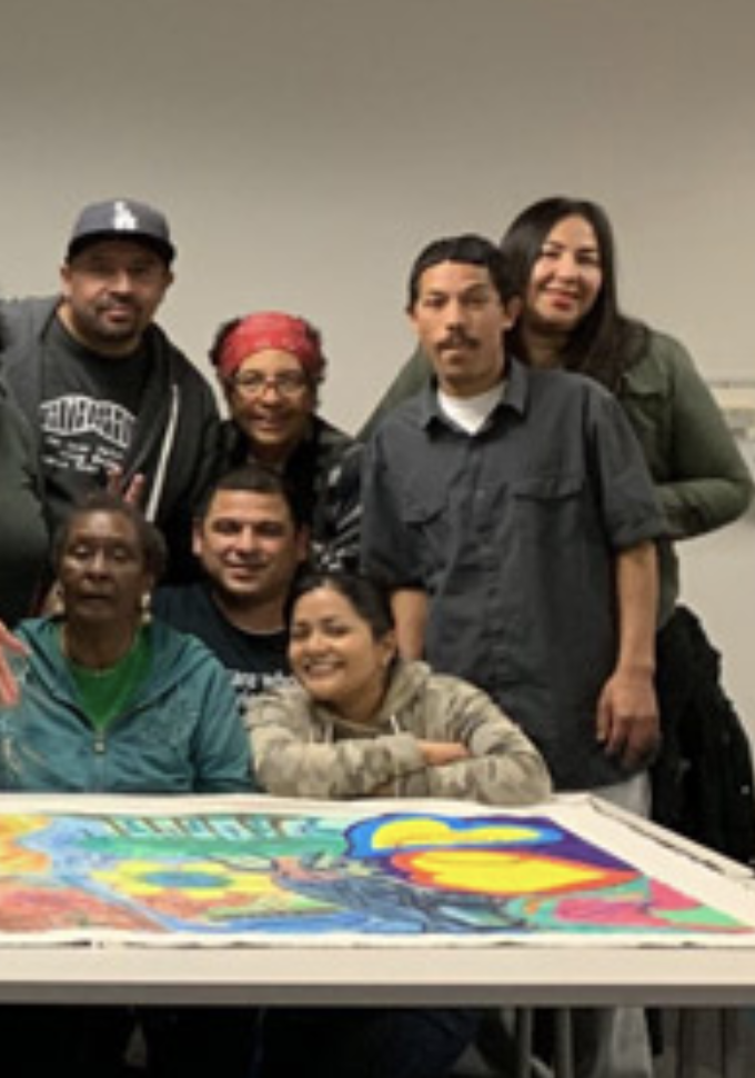 Students from the Bridge Program standing a classroom with a brightly colored tapestry in front of them. 
